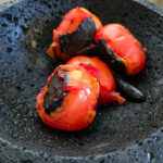 Lägg tomaterna och en av de rostade chilifrukterna i en blender eller molcajete
