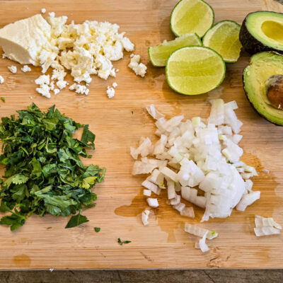 Smula ost, finhacka lök och koriander, skär klyftor av lime och gör kuber av avokado.